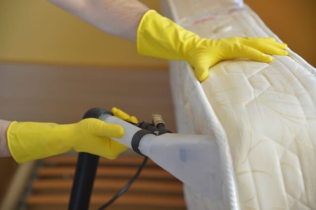 mattress being deep cleaned with shampoo suction pump by cleaner wearing yellow gloves